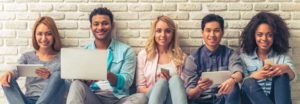 Young people of different nationalities smiling, sitting against white brick wall