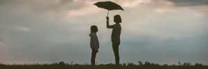 silhouette of woman holding umbrella standing in front of girl on hill